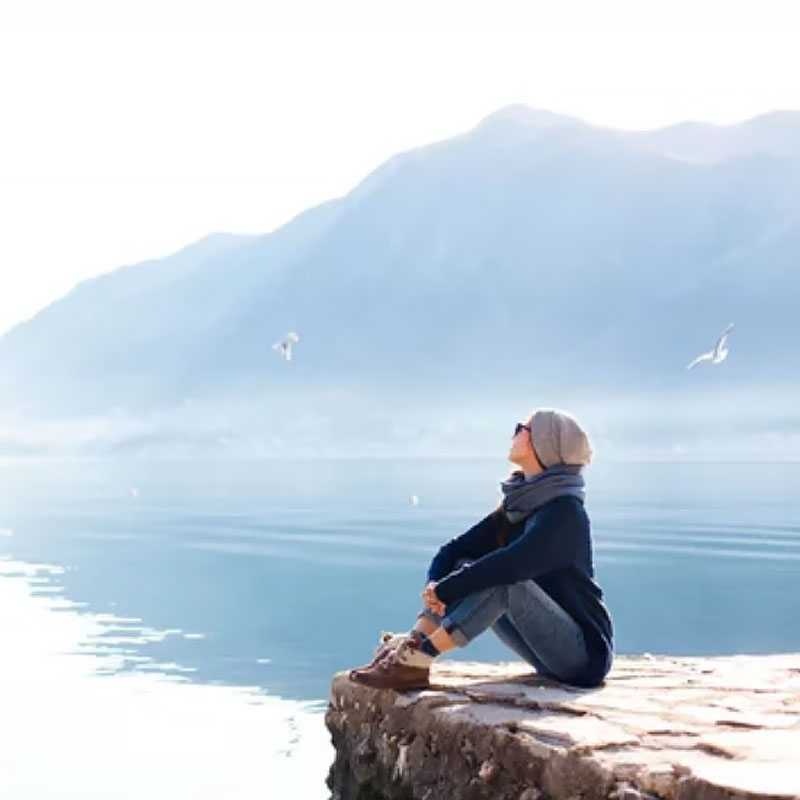 A women sitting on a rock looking out at the water and thinking about christina-rella-craniosacral-therapist-nelson-bc